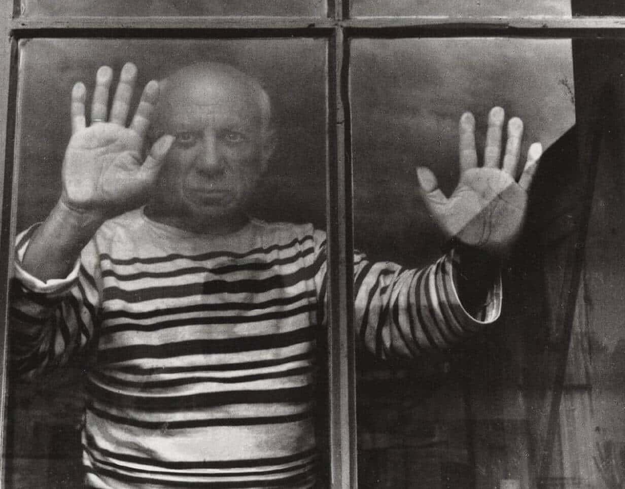 A photo of Picasso standing behind a window with his hands pressed up against the glass. It's interesting to see the palms of his hands.
