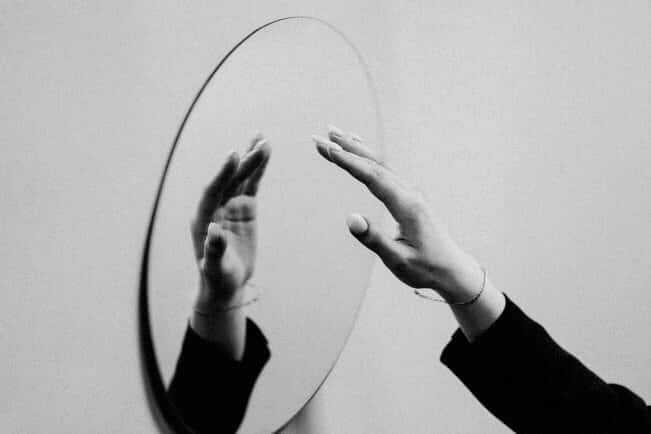 Image of a person reaching out to a mirror, their hand reflected.